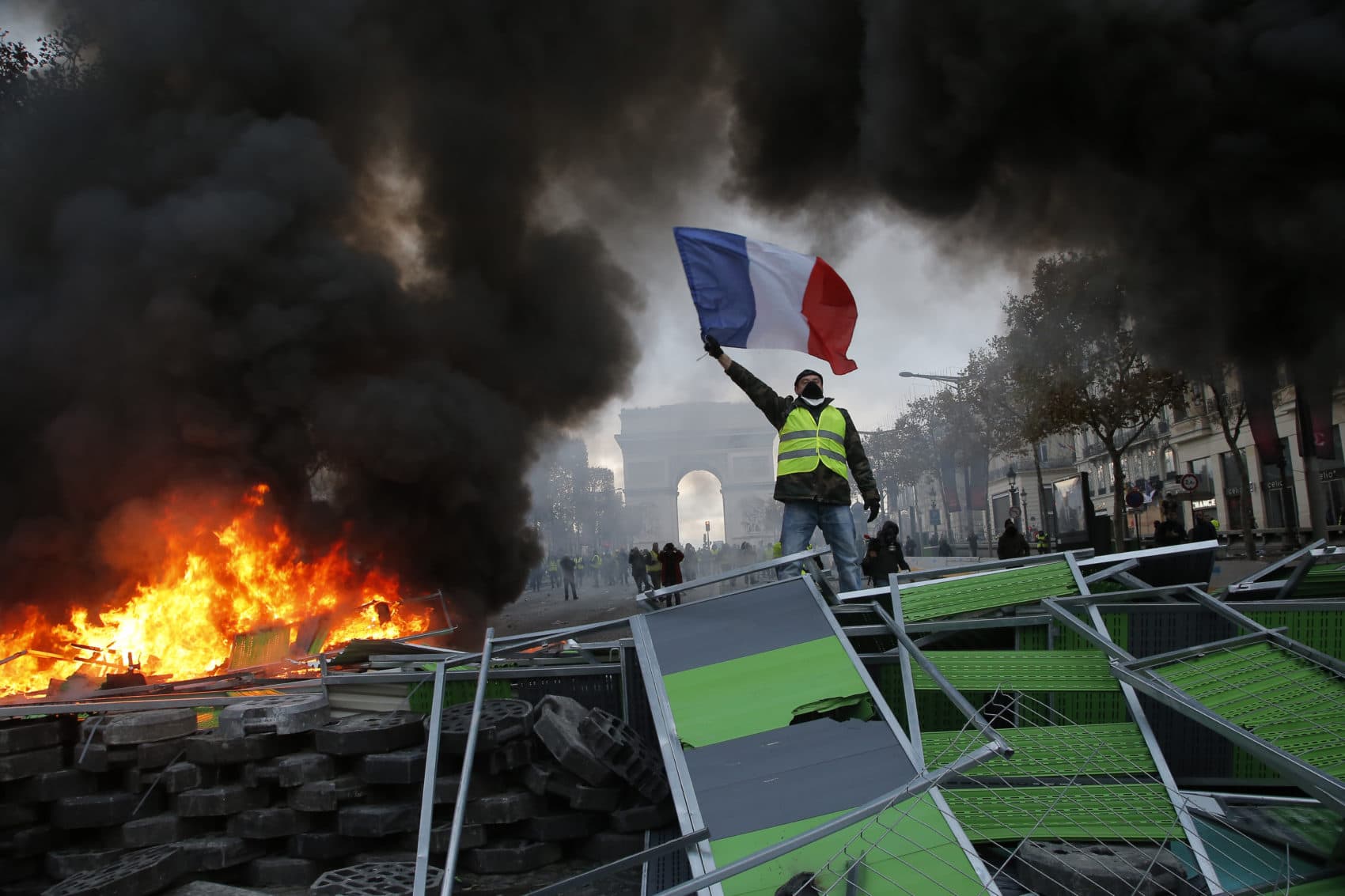 A demonstrator waves the French flag onto a burning barricade on the Champs-Elysees avenue during a demonstration against the rising of the fuel taxes, Saturday, Nov. 24, 2018 in Paris. (Michel Euler/AP)
