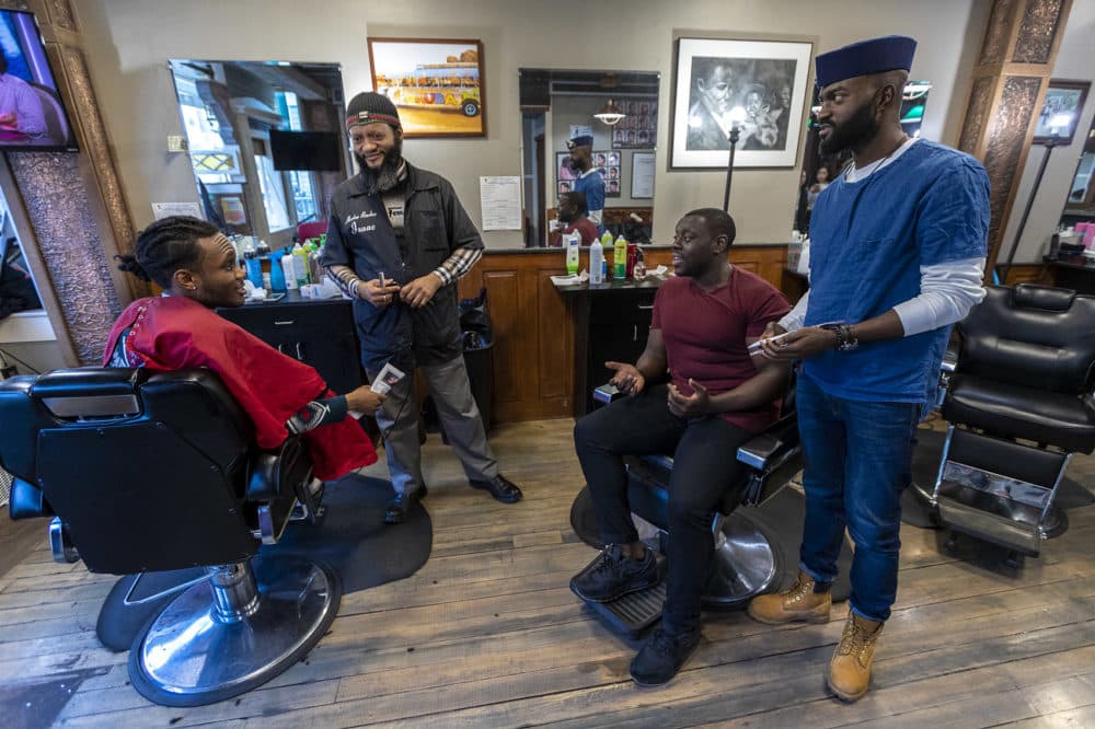 From right to left: Bright Genty and his father, master barber Isaac, speak with &quot;Barber Shop Chronicles&quot; actor Ekow Quartey and the production's writer Inua Ellams at Headlines Unisex Barbershop in Cambridge. (Jesse Costa/WBUR)