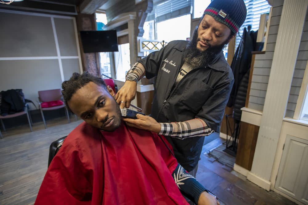 Master barber Isaac Genty trims the beard of his son Bright, who is training to become a barber himself at Headlines Unisex Barber Shop in Cambridge. (Jesse Costa/WBUR)