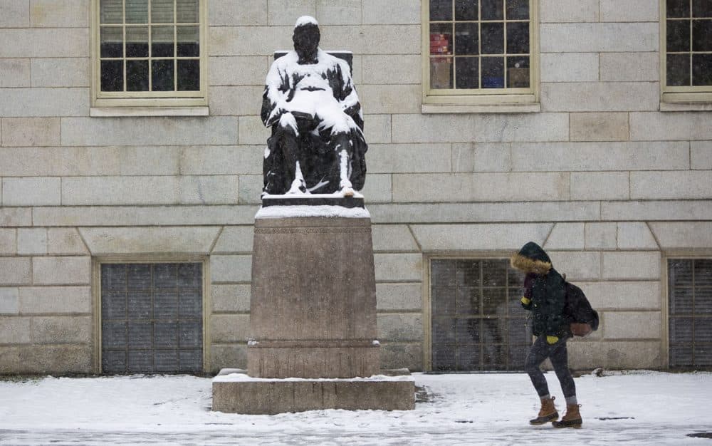A student on her way to class passes a snow covered John Harvard in Harvard Yard on Monday, April 4, 2016. (Jesse Costa/WBUR)