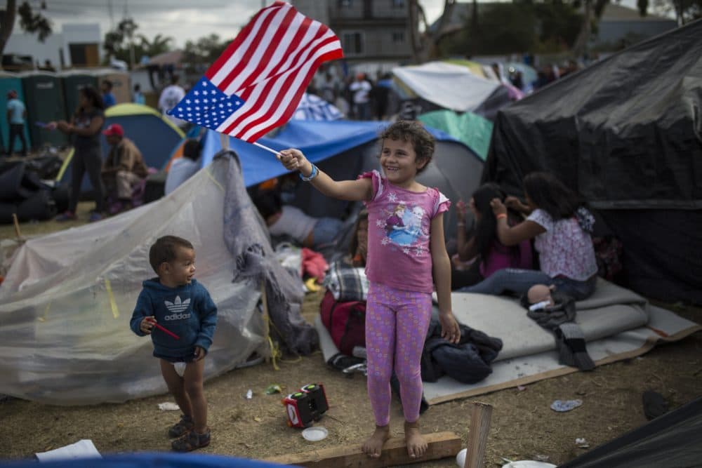 Seven-year-old Honduran migrant Genesis Belen Mejia Flores waves an American flag at U.S. border control helicopters flying overhead near the Benito Juarez Sports Center serving as a temporary shelter for Central American migrants, in Tijuana, Mexico, Saturday, Nov. 24, 2018. (Rodrigo Abd/AP)