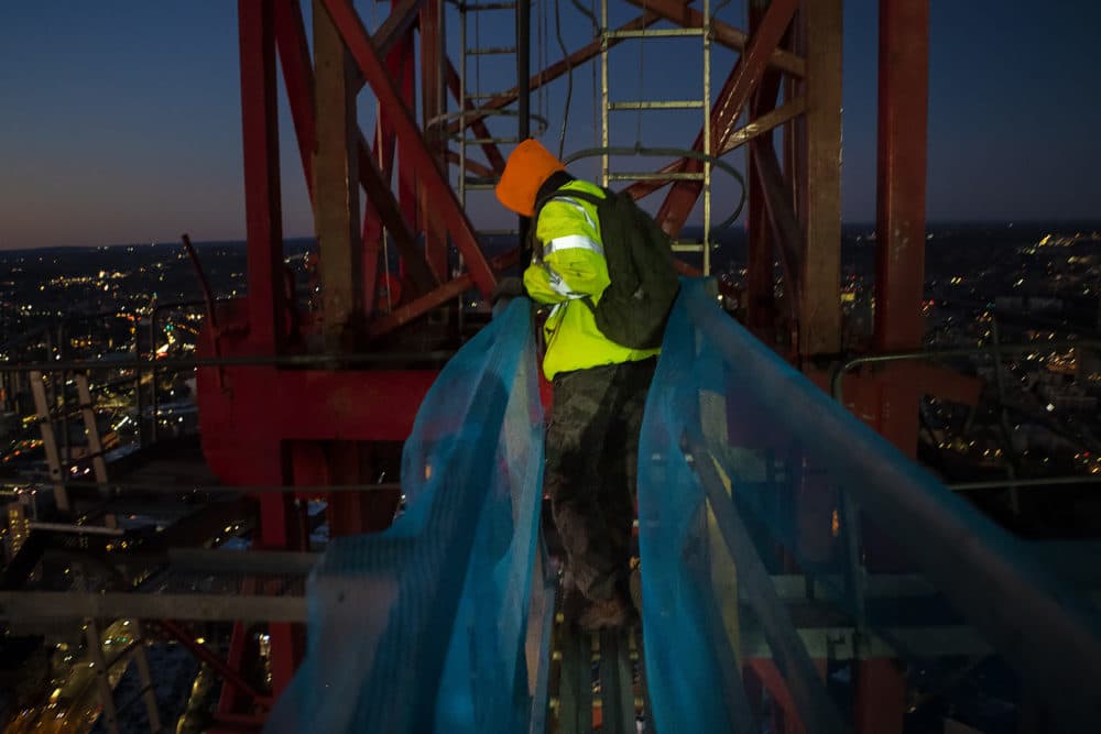 Crane operator Brett St. Germain looks down as he crosses a bridge from One Dalton's 61st floor to the mast of the crane to begin his workday. He'll have to climb five 16-foot ladders before climbing into the crane's cab. (Jesse Costa/WBUR)