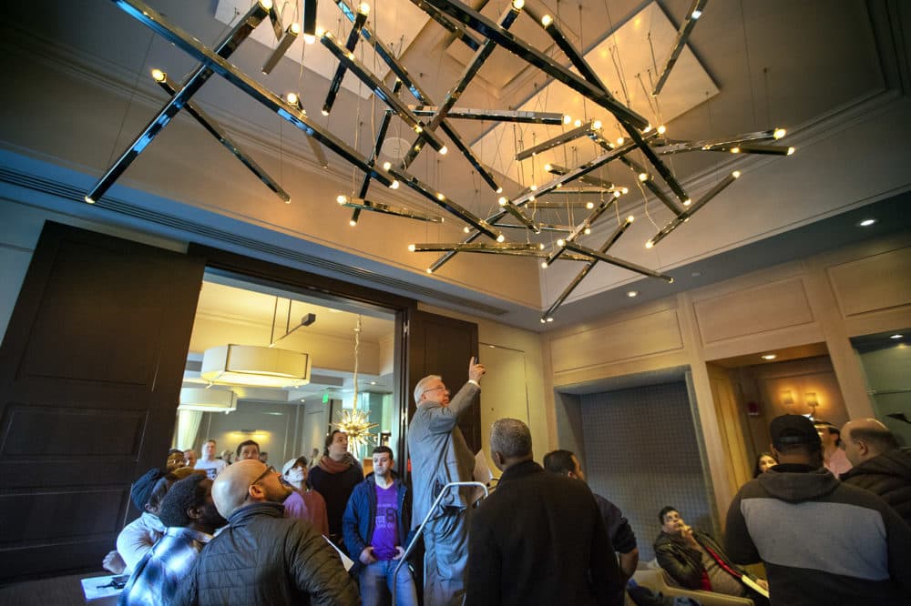 Auctioneer Ed Smith points up to the large chandelier in the entrance of L’Espalier Restaurant to begin the bidding by participants. (Jesse Costa/WBUR)
