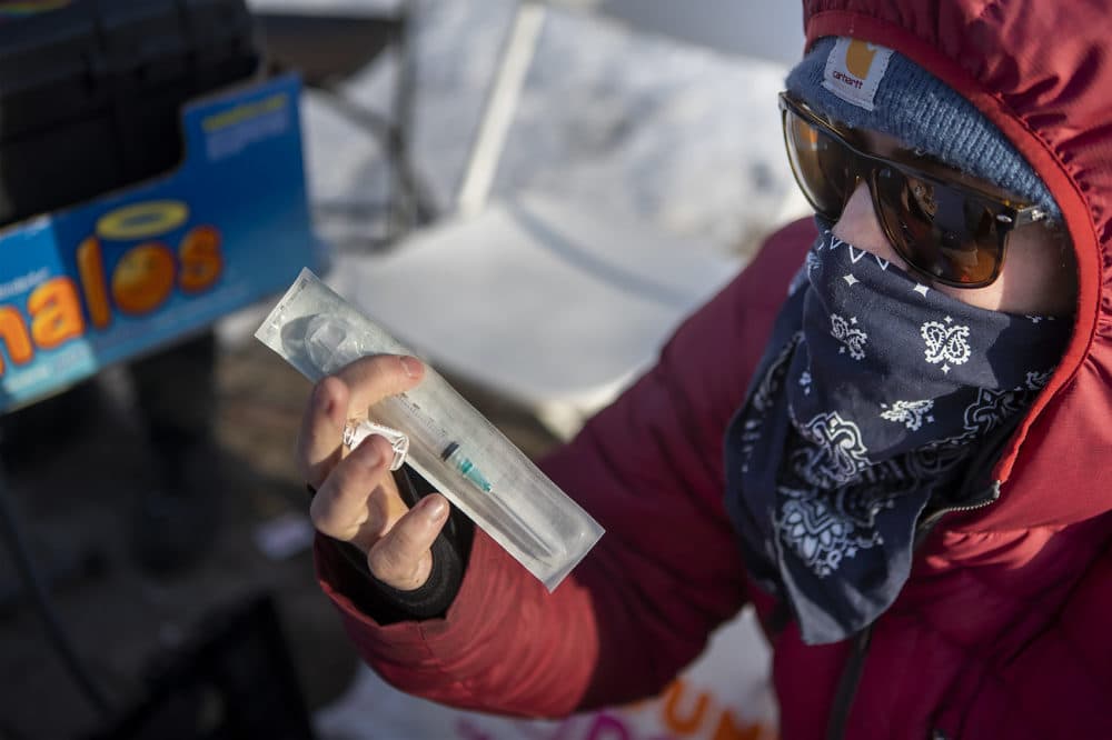 A man who identifies as Dave Carvagio holds a packaged needle in Pickering Square in Bangor, Maine. The Bangor chapter of Church of Safe Injection sets up a table in the square and offers users needles, free Narcan and other drug injection-related paraphernalia. (Jesse Costa/WBUR)