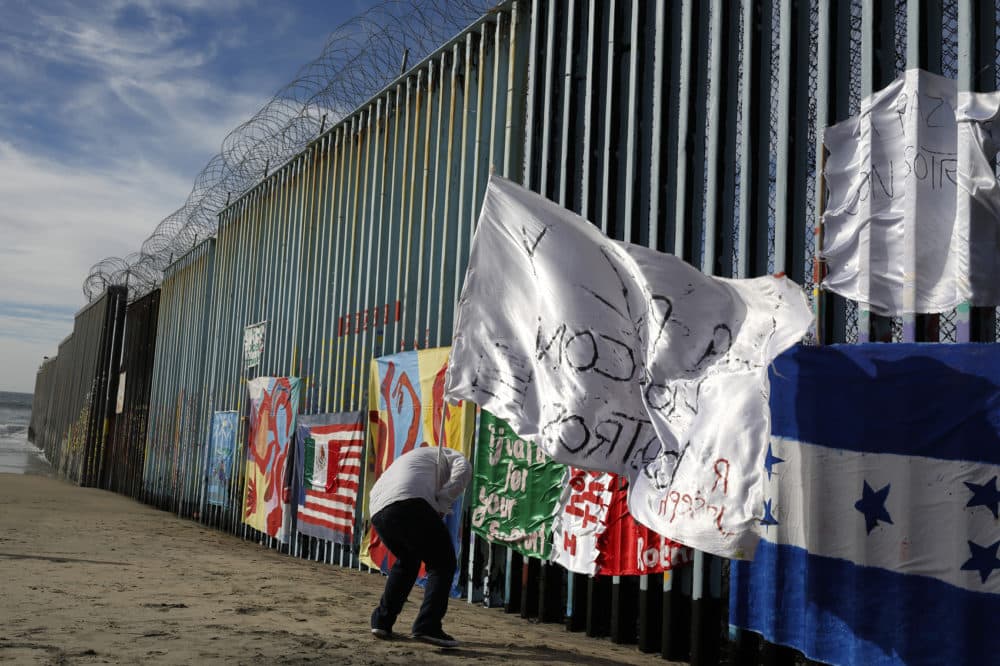 Joseph, an migrant from Honduras, plants a white flag with the words, &quot;peace and God with us,&quot; in front of the border wall during an art display on the border wall, topped with razor wire, Tuesday, Jan. 8, 2019, on the beach in Tijuana, Mexico. (Gregory Bull/AP)