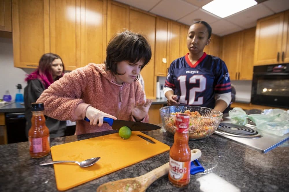 Under the watchful eye of College Success resident staff worker Brandi Cooley, right, student Jordan Scheffer carefully cuts a lime in half to use the juice in the pico de gallo she is making for their Super Bowl watch party. (Jesse Costa/WBUR)