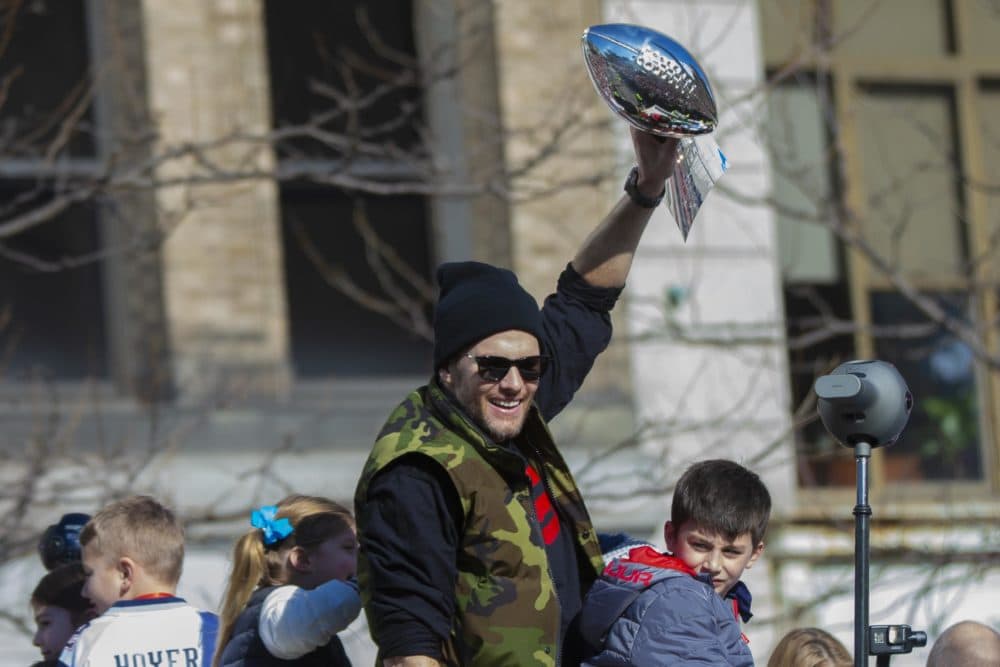 Patriots quarterback Tom Brady lifts the Lombardi trophy above his head as the rolling rally heads down Boylston Street on Tuesday. (Jesse Costa/WBUR)