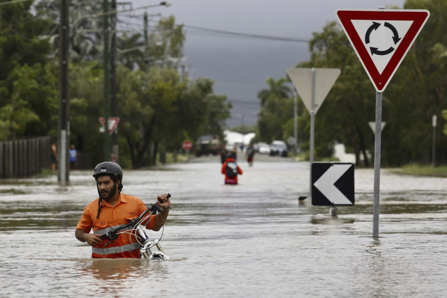 In this Sunday, Feb. 3, 2019, photo, a resident pushes a bicycle through floodwaters at Hermit Park in Townsville, Australia. More than 1,100 people had been rescued from their homes on Sunday night and evacuation efforts were continuing Monday. (Andrew Rankin/AAP Image via AP)