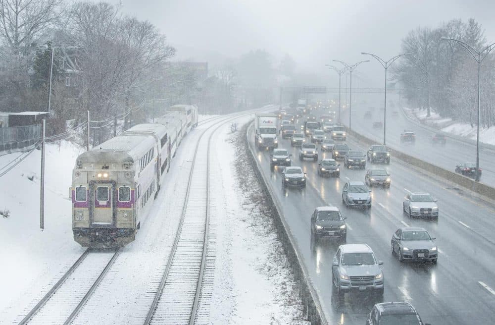 A commuter rail train and vehicles on the Mass. Turnpike make their way through light snow during the morning commute. (Robin Lubbock/WBUR)