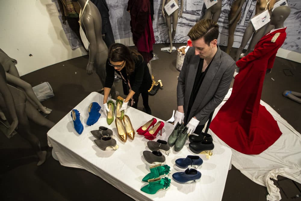 The MFA Boston's “Gender Bending Fashion” exhibition curator Michelle Finamore, left, and shoe designer and Newton native Thom Solo place shoes on a table that they will use to accessorize the mannequins in the show. (Jesse Costa/WBUR)