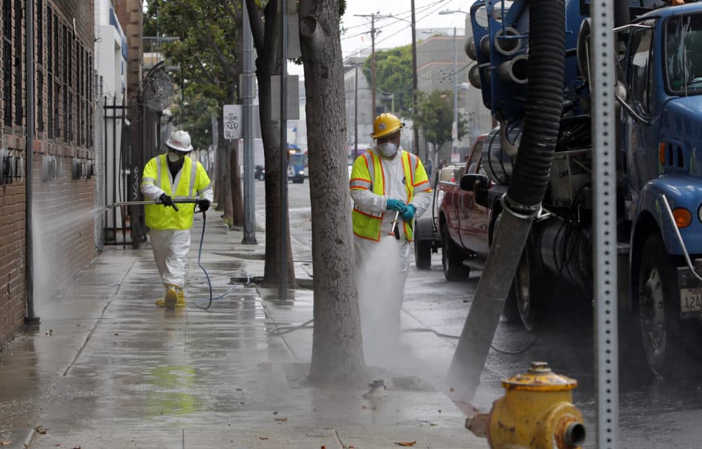Sanitation workers in protective suits clean a street in the heart of the Skid Row district in downtown Los Angeles in 2012, amid a typhus outbreak. (Nick Ut/AP)