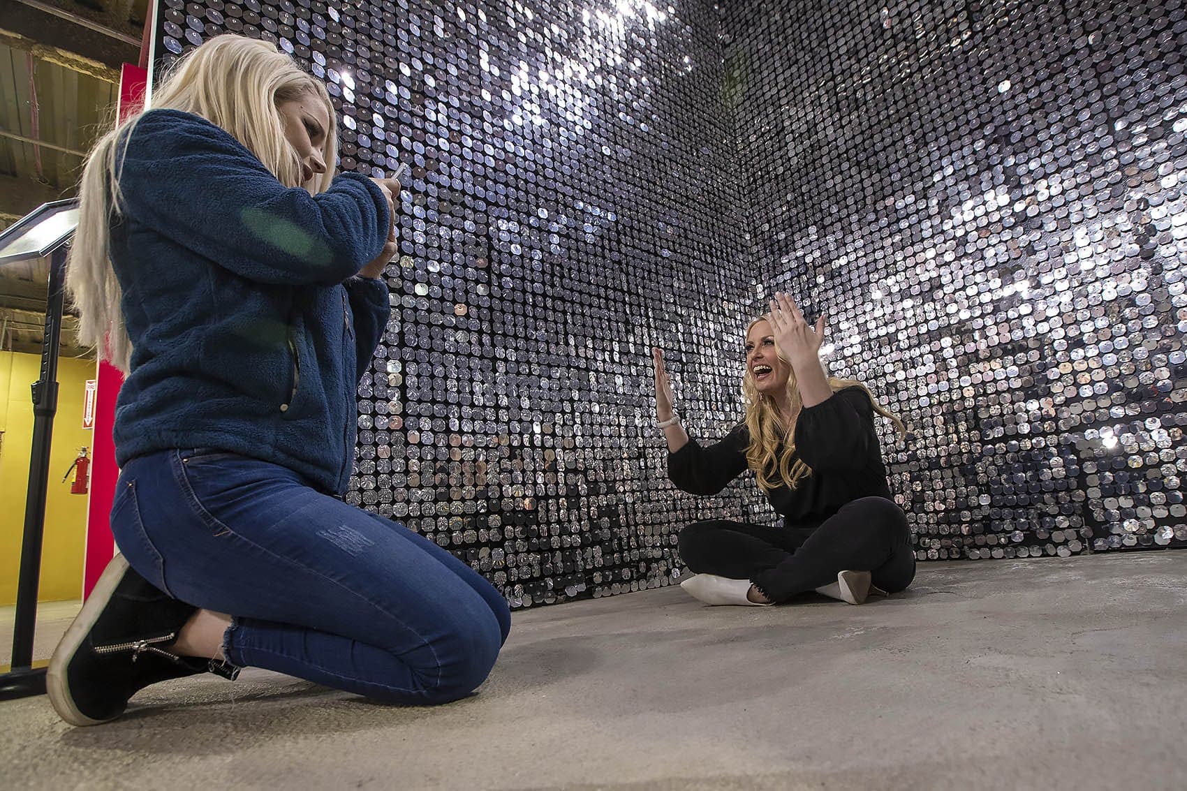 Caroline Gray takes a photo of Sarah Russo with her phone in the glittery space at “Happy Place.” (Jesse Costa/WBUR)
