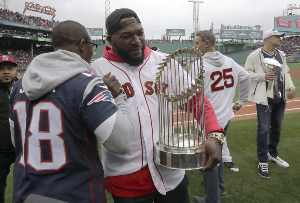 New England Patriots' Matthew Slater, left, clasps hands with former Boston Red Sox star David Ortiz as he holds the World Series trophy before the home opener. At right are former Red Sox star Mike Lowell (25) and retired New England Patriots' Rob Gronkowski, far right. (Charles Krupa/AP)