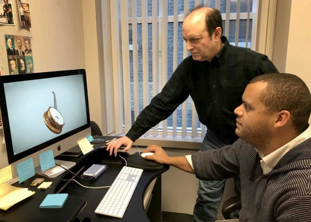 Shaun Clarke sits at the computer, showing 3D model of a pre-Civil War banjo, while Marc Fields looks on. (Andrea Shea/WBUR)