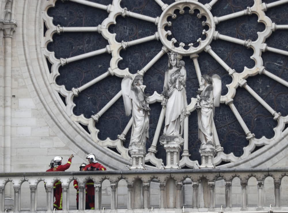 Firefighters talk near the rose window of Notre Dame cathedral Tuesday April 16, 2019 in Paris. Experts assessed the blackened shell of Paris' iconic Notre Dame to establish next steps to save what remains. (Thibault Camus/AP)