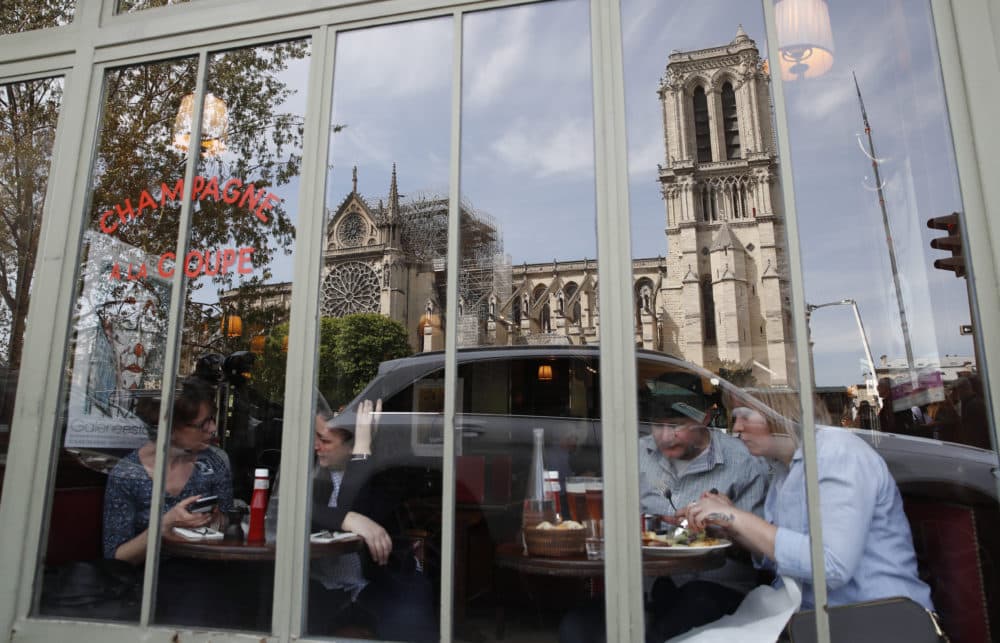 People eat at a cafe with the Notre Dame Cathedral reflected in the window in Paris, Thursday, April 18, 2019. (Christophe Ena/AP)