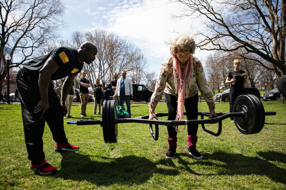 Jadwiga Serafin, of Poland, is coached by Sgt. First Class Anthony Darrison while trying the dead lift at Boston Common. Serafin, who is 62, exclaimed, “This is nothing!” and asked for more weight. (Erin Clark for WBUR) 