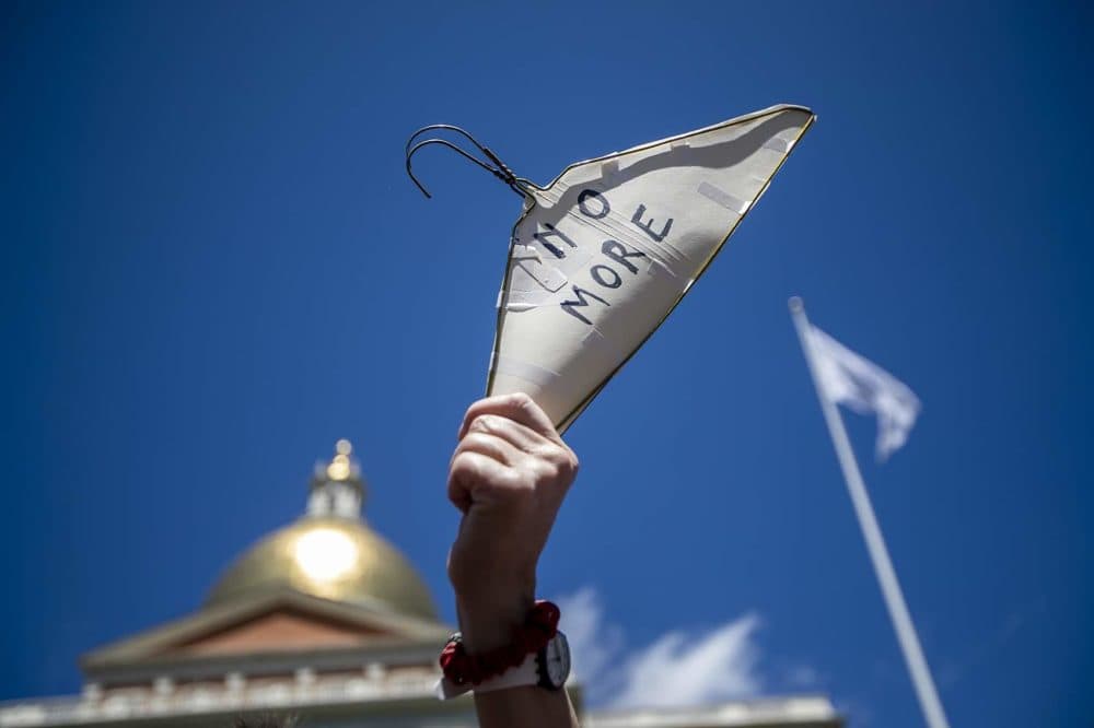 Viviana Planine holds up a coat hanger with the words “No More” inscribed on it during the #StopTheBans rally at the State House. (Jesse Costa/WBUR)