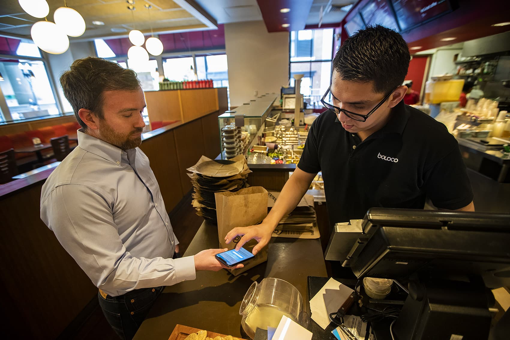 Boloco manager Erick Guitierrez taps Tom Leonard’s phone as he purchases a breakfast burrito with the “Food For All” app. (Jesse Costa/WBUR)