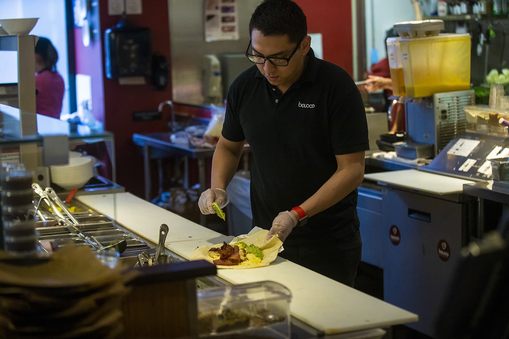 Boloco manager Erick Guitierrez slaps some guacamole onto a breakfast burrito he is making for a customer using the “Food For All” app. (Jesse Costa/WBUR)