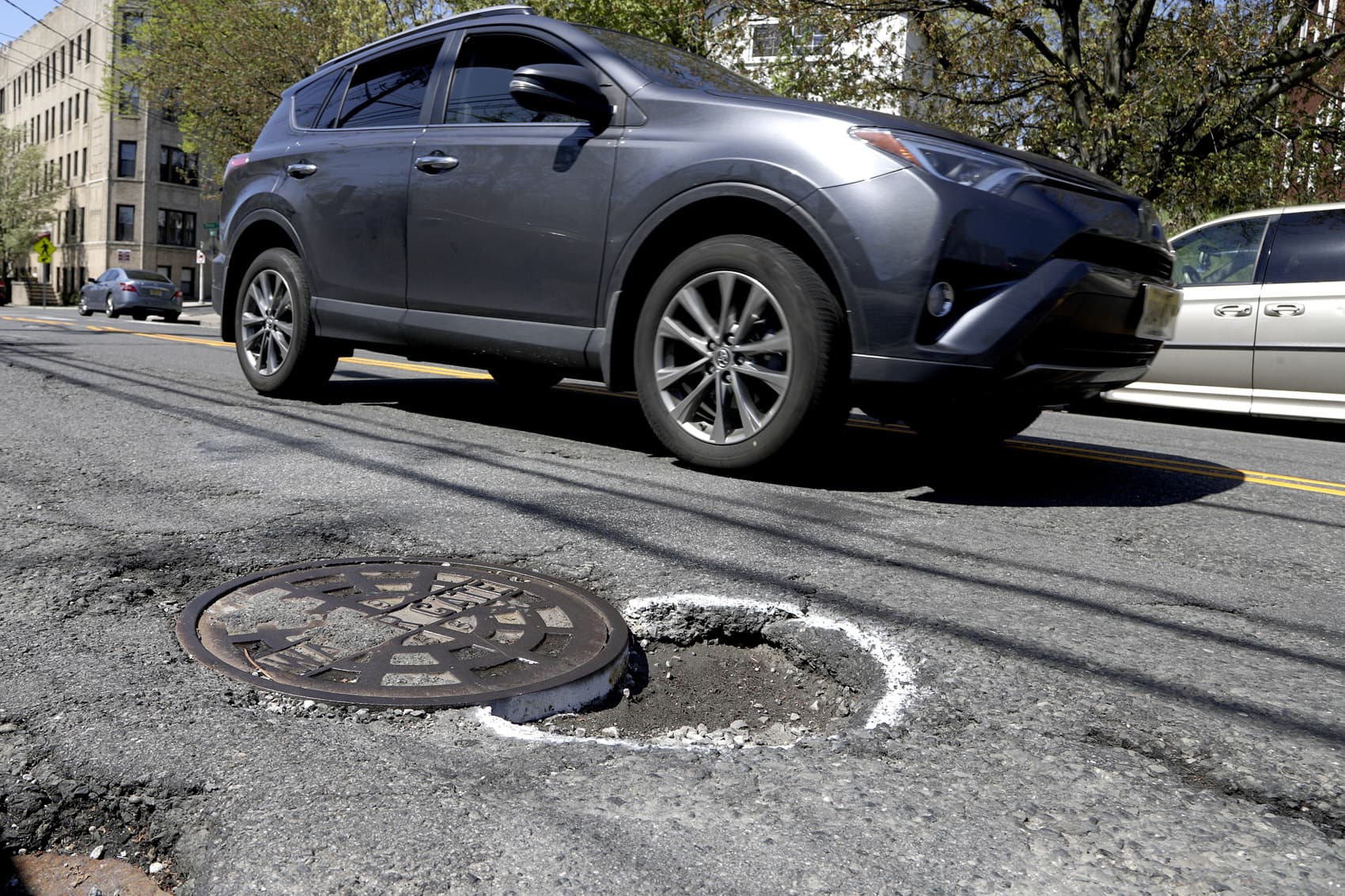 A vehicle maneuvers around a pothole outlined by paint near a manhole along Summit Avenue, Tuesday, April 23, 2019, in Jersey City, N.J. (Julio Cortez/AP)