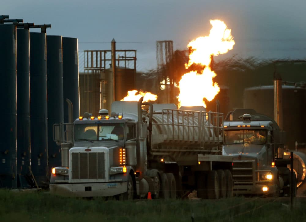 In this June 9, 2014 file photo, drivers and their tanker trucks, capable of hauling water and hydraulic fracturing liquid, line up near a natural gas burn off flame and storage tanks in Williston, N.D. (Charles Rex Arbogast/AP)
