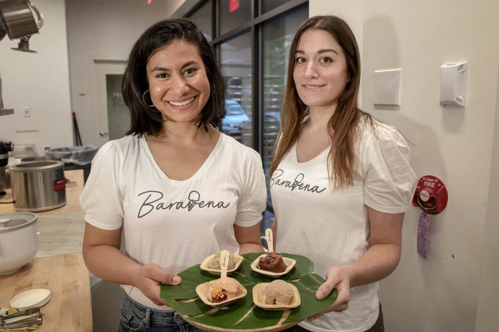 Baravena's Nayla Bezares stands with her partner Sylvia Berciano Benitez. The two doctoral students at Tufts show the various helado flavors they've concocted from oats. (Robin Lubbock/WBUR)