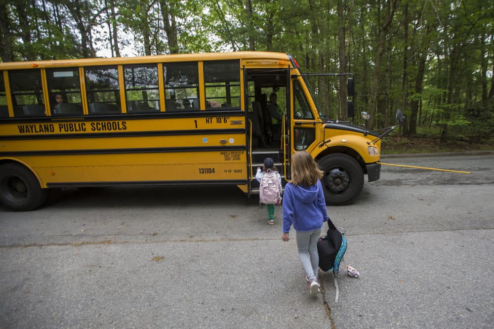 Anya, foreground, and a friend board their Wayland school bus. The town's school start times are set to shift. (Jesse Costa/WBUR)