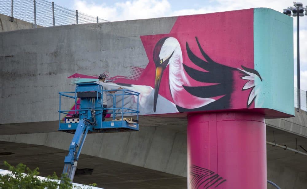 High up on a beam supporting I-93, muralist Victor &quot;Marka27&quot; Quiñonez works the crane at the top of his new piece. (Robin Lubbock/WBUR)