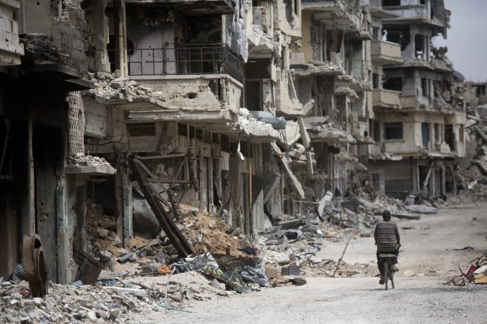 In this June 5, 2014, file photo, a man rides a bicycle through a part of Homs, Syria, devastated by the country's civil war. Numerous studies have suggested climate change was a factor in record setting drought in Syria -- one of several causes of the country’s civil war that triggered a massive refugee crisis. (Dusan Vranic/AP)