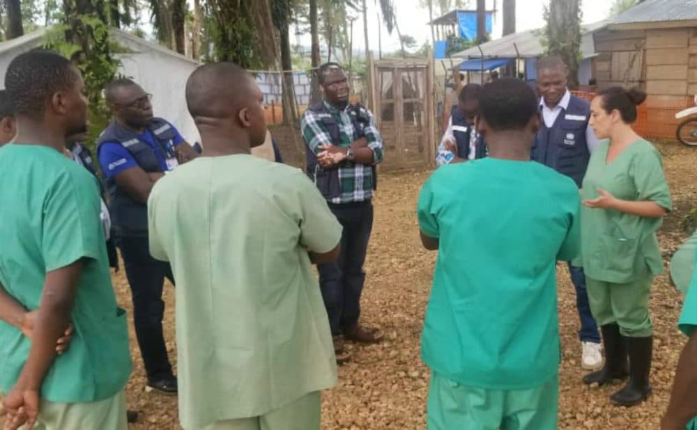 Dr. Marta Lado (far right), who is on leave from her job as chief medical officer of Partners In Health Sierra Leone, and a team of Congolese doctors (also in scrubs) discuss the challenges at an Ebola treatment center in Mangina, DRC with representatives from the World Health Organization. (Courtesy Dr. Marta Lado)