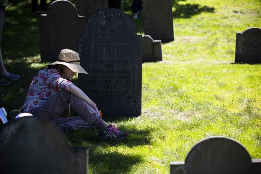 A woman sits in the shade at an unveiling ceremony of the Medford Slavery Memorial in Salem Street Burying Ground. (Erin Clark for WBUR)