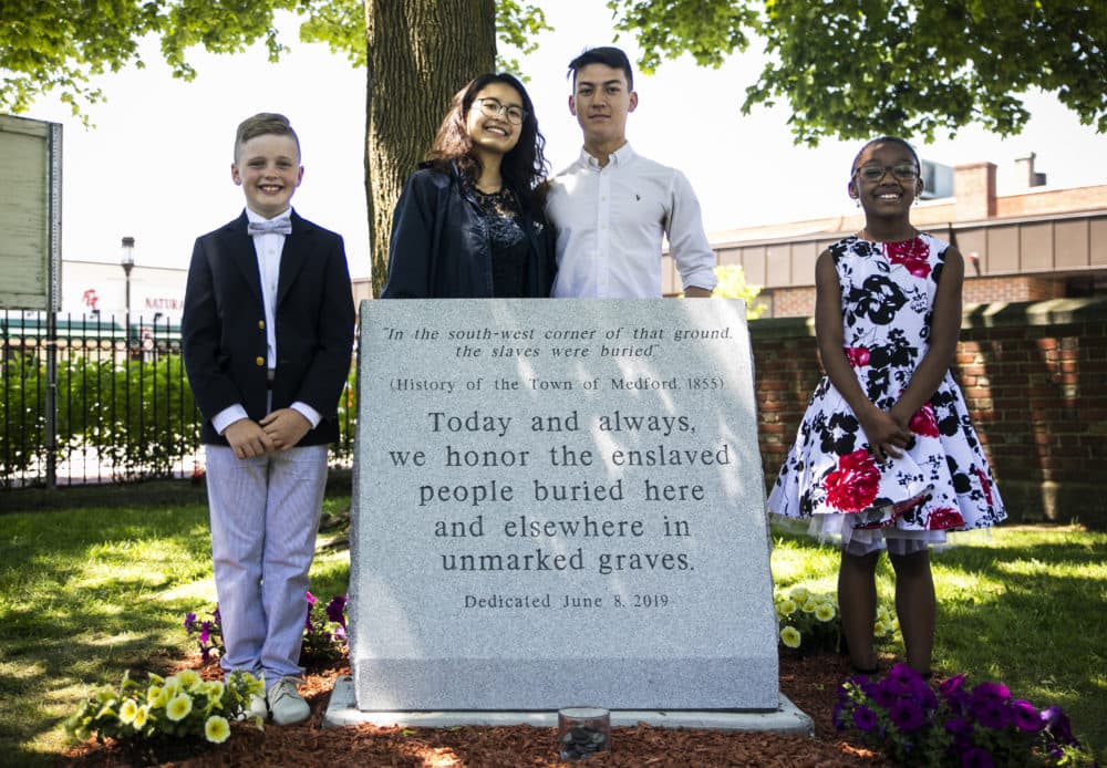 Medford Public Schools students Liam Brady, Jenny Lu, Joseph Schmidt and Jasmine Hagbourne stand for a photo at the unveiling ceremony of the Medford Slavery Memorial in Salem Street Burying Ground. The students organized the creation of a memorial to a group of more than 50 slaves who were buried in unmarked graves in the Salem Street Cemetery. (Erin Clark for WBUR)