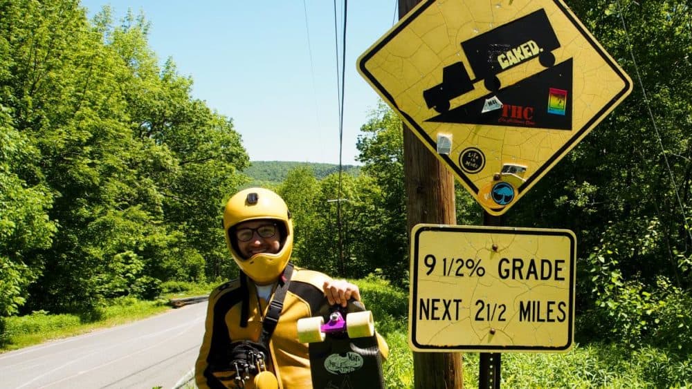Jack Collins of Harrisburg, Pennsylvania, has been skating downhill for six years. Here he stands next to a road-grade sign on Whitcomb Hill Road in Florida, Massachusetts. (Ben James/NEPR)
