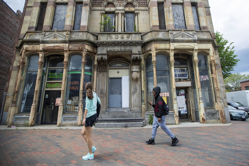 A woman looks up at the old dilapidated Alexandria Hotel on Washington St. Boston officials classified the redevelopment as a South End project, but the building is actually in Roxbury. (Jesse Costa/WBUR)