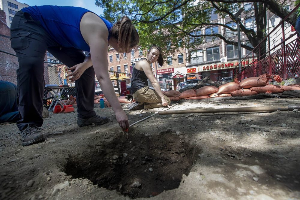 Lauryn Poe, right, and Sarah Keklak measure to create a 6 foot x 3 foot trench. They are trying to locate the rear of a building erected in 1841 that once stood on the property at 6 Hudson St. during the first archaeological dig in Boston's historic Chinatown. (Jesse Costa/WBUR)