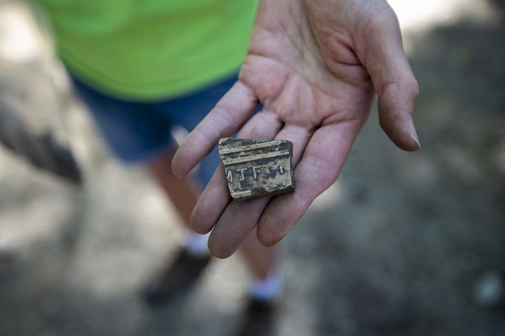 A piece of tile with markings on the back is an interesting find. The archaeologists will look up the letters and numbers to find who the manufacturer was and when it was made. (Jesse Costa/WBUR)