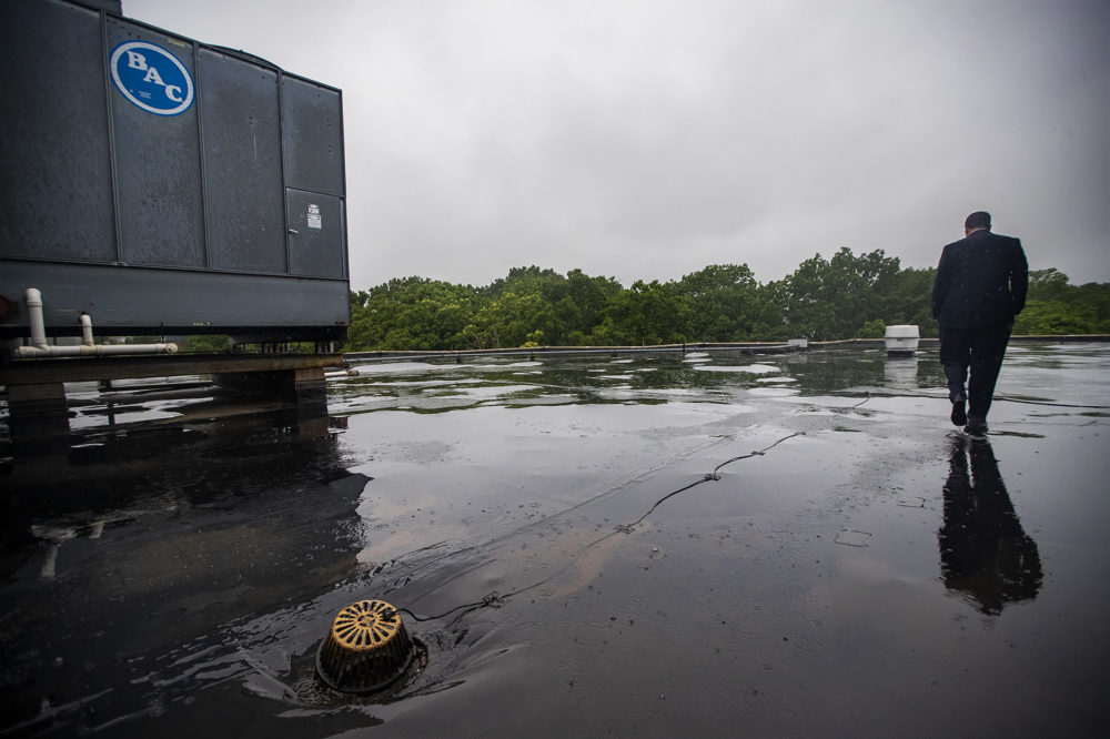 Hanlon walks in the rain through the puddles collecting on the billowing roof of the school building. (Jesse Costa/WBUR)