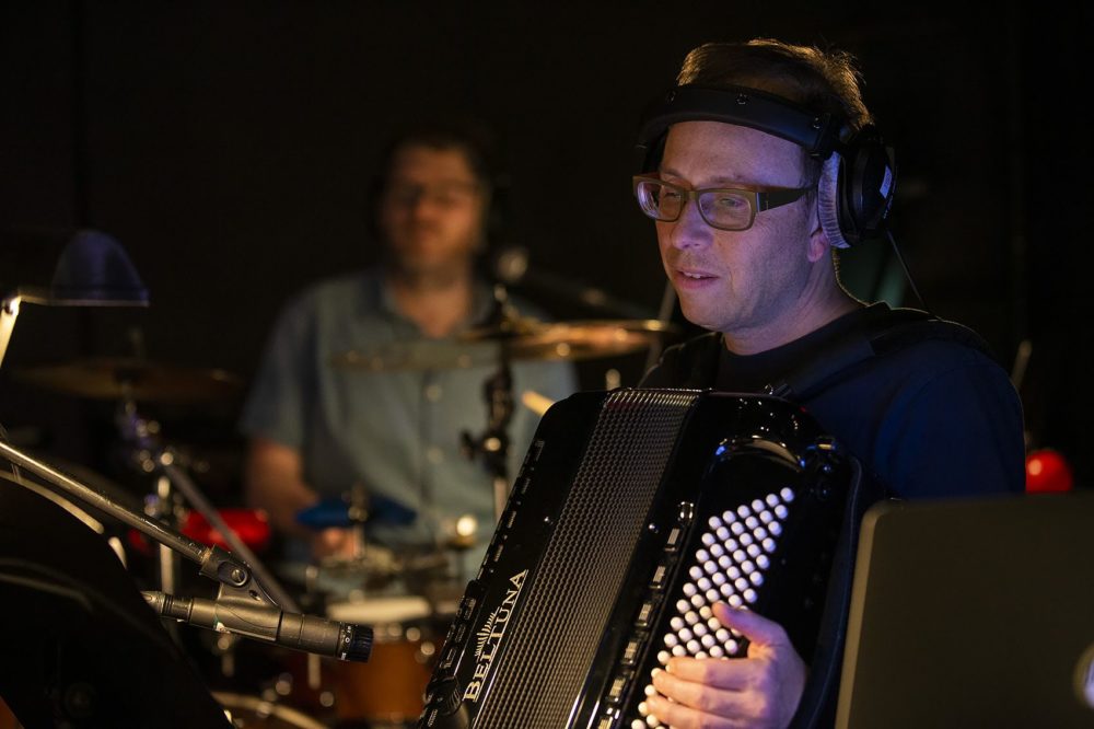 Peter Bufano plays his accordion as Mike Dobson plays drums in the background. (Jesse Costa/WBUR)