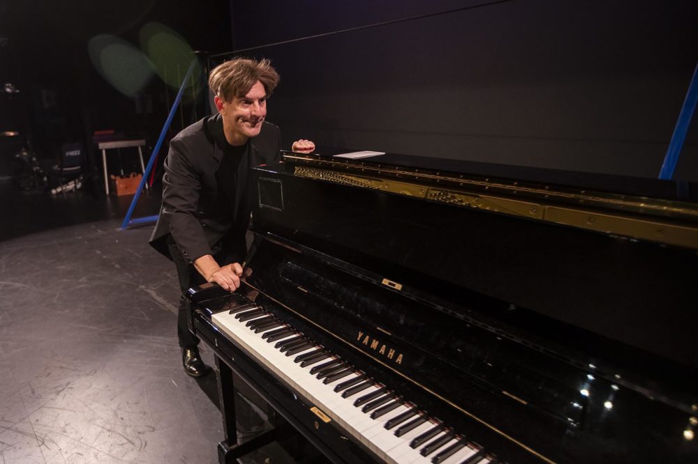 Comedian Joel Jeske pushes a piano across the stage. (Jesse Costa/WBUR)