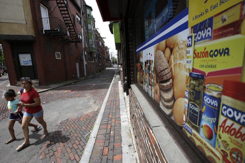 Passers-by walk on a side street near a store front that features images of Latin foods, in Chelsea, Mass. (Steven Senne/AP)