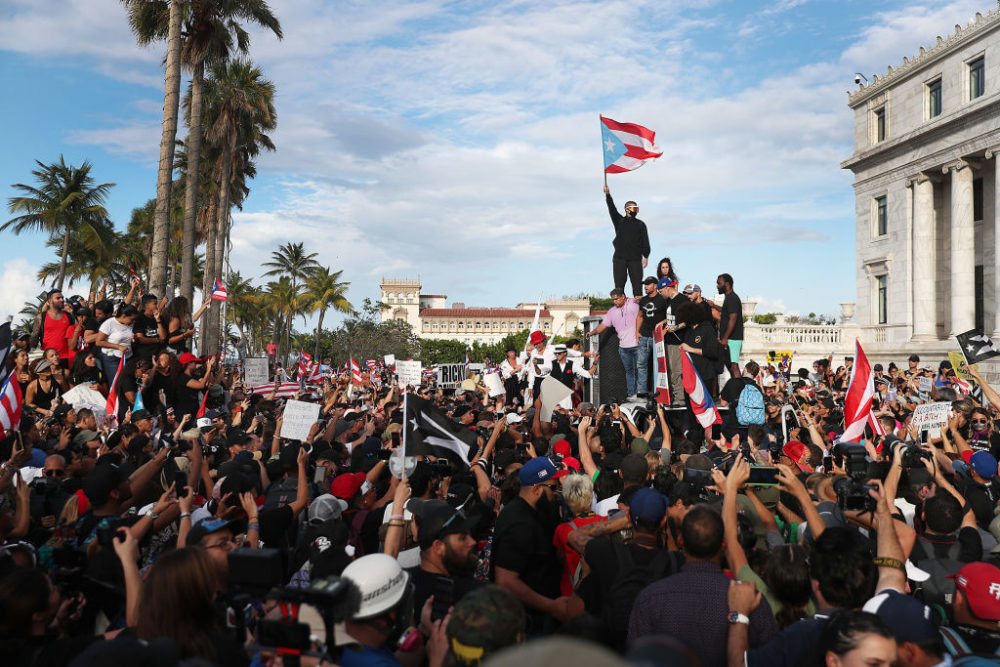 Rapper Bad Bunny (holding flag), singer Ricky Martin (black hat) and rapper Residente (blue hat) join demonstrators protesting against Ricardo Rosselló. (Joe Raedle/Getty Images)
