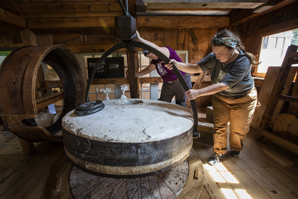 Kim VanWormer, right, and Sydney Tierney carefully move the 2500 lb. mill stone into place. (Jesse Costa/WBUR)