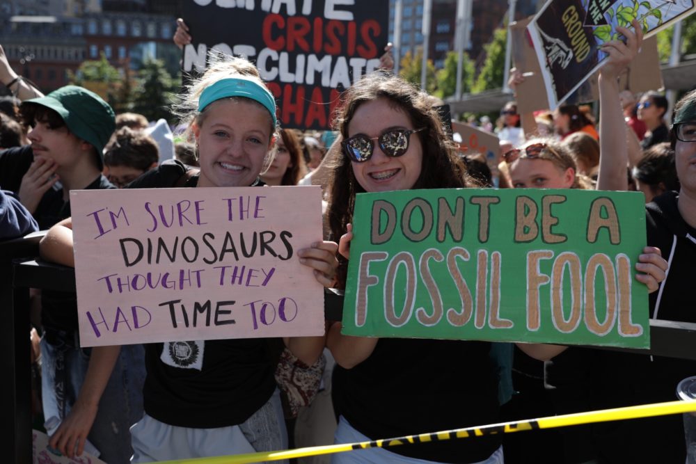 Two young climate activists hold up signs during the protest. (Robin Lubbock/WBUR)