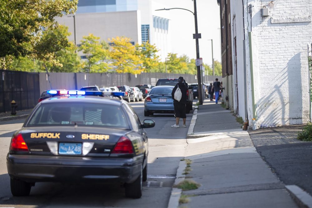 A group of homeless people walk away after a Suffolk County sheriff’s police car pulls up to the side of the road on Bradston Street. (Jesse Costa/WBUR)