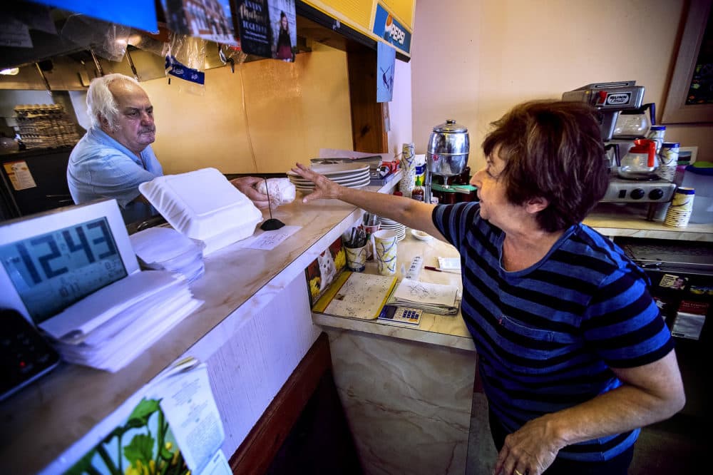 Charlie Christopoulos pasa el sandwich para un cliente a su esposa Theodora en el local Charlie's Junction de Downtown Lynn. (Jesse Costa/WBUR)