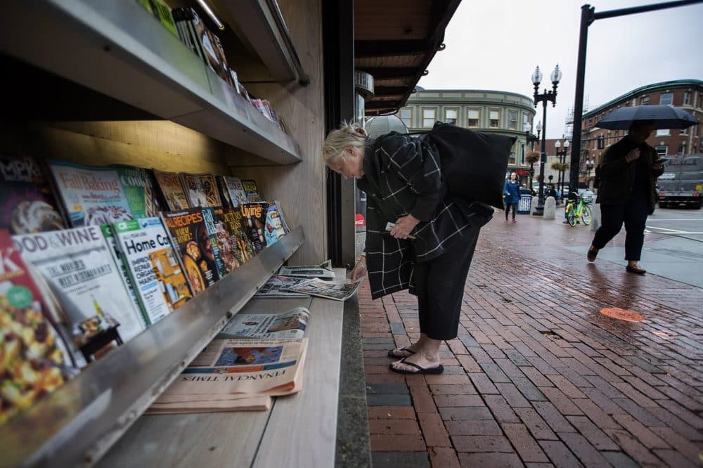 A woman looks at the front page of the New York Daily News outside the newsstand of Out of Town News, which once was brimming with publications. (Jesse Costa/WBUR)