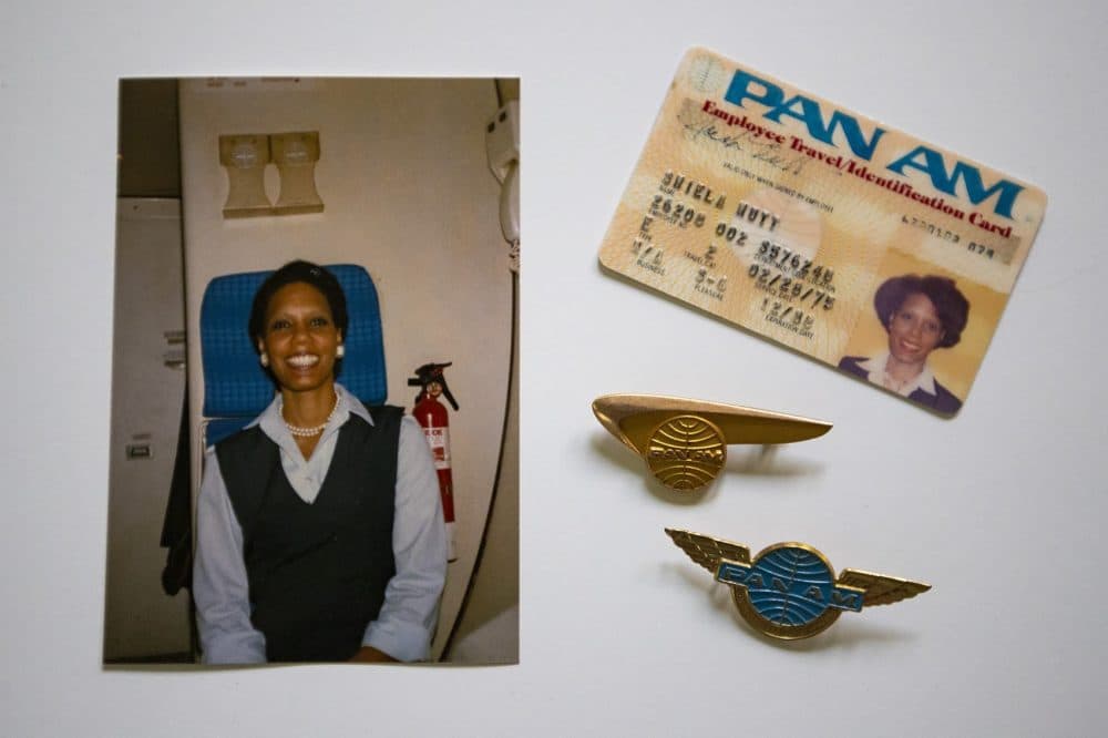 A photograph of Shelia Nutt onboard a Pan Am Airlines jet from 1985, her Pan Am Identification card, and two Pan Am pins. (Jesse Costa/WBUR)