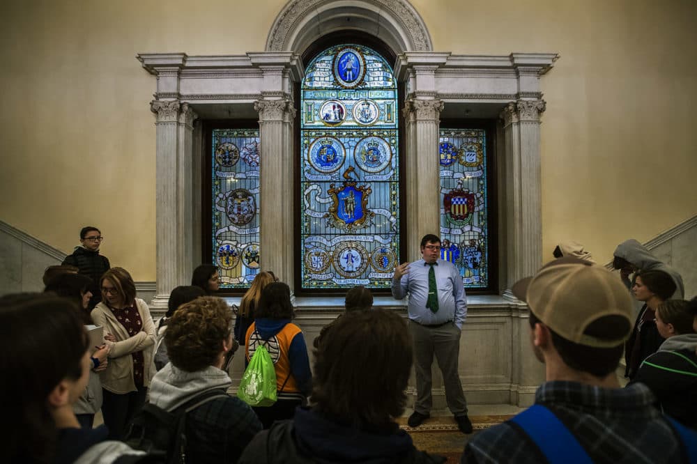 A tour group inside the Massachusetts State House is shown a stained glass display with the “Seal of the Commonwealth” located at the top of the grand staircase. (Jesse Costa/WBUR)