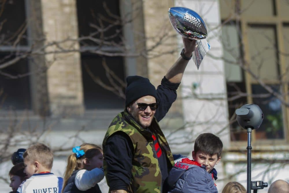 New England Patriots quarterback Tom Brady lifts the Lombardi trophy above his head as the Patriots Rolling Rally heads down Boylston St. (Jesse Costa/WBUR)